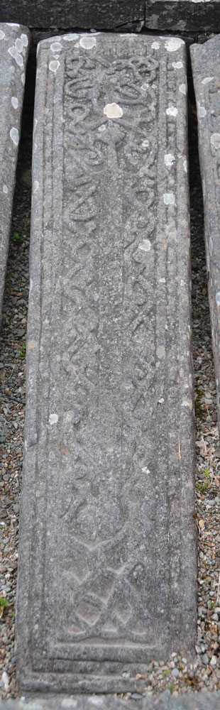 This tapered slab in the Poltalloch Enclosure measures 1.83m by 0.44m. It has linked plant stems above a pair of animals; these flank a sword blade which has had a previous inscription obliterated from it.  The name POLTALLOCH has been cut into a panel at the top. Loch Awe School. 14th to 15th century.