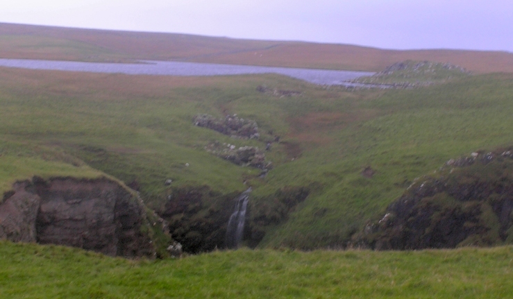 View of Loch of Houlland from the west back over the Holes of Scraada.Looking inland over the Holes of Scraada and the Loch of Houlland, the broch can be seen above a line of ruins.  These are 3 'horizontal mills' which were powered by the outlet from the loch, a common feature on burns in Shetland.From the size of many stones in the mills, it seemed quite likely that much building material might 