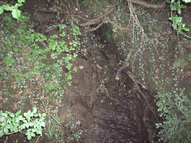 St Oswald's Well in the gloom. Some old brickwork can be seen.

