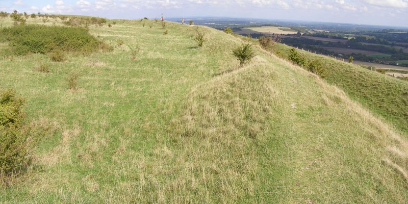 Panoramic photo of the eastern side of the hillfort, with the ramparts and ditch to the right. Immediately to the left of the inner rampart the ground has many shallow hollows - probably infilled quarry pits from the construction of the ramparts. There are remains of hut circles elsewhere within the hillfort's interior.