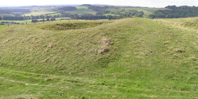 Panoramic photo of the earthworks to the west of the original entrance at the southeast corner of the hourglass-shaped hillfort. The inner rampart turns in at the entrance and the outer rampart also turns inwards and meets the inner rampart.