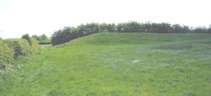 This hilltop mound is hidden from the road by a high hedge. It is near to the Download Music Festival Camp Site, near the western runway lights of East Midlands Airport, and adjacent to a Severn-Trent water works. Nearby an Iron Age field system was excavated in preparation for Airport buildings.
It is 48m long, 17m wide, and 1 & 1/2m high at the eastern end. Is it a known long barrow?
Location: