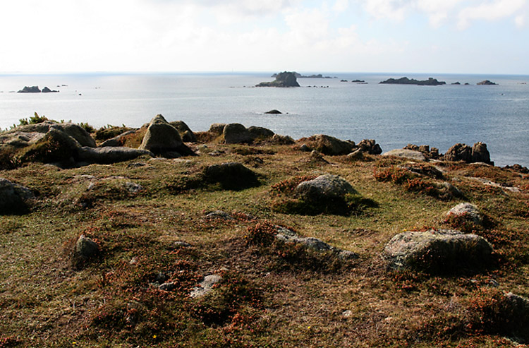 This view looks south over the southwestern cairn of the three on Gweal Hill. 
The central cist can be seen centre-left, and there are two rings of kerbs both of which can just be seen on this photo, although the whole mound is now greatly weathered by its position on the most westernmost point of the inhabited islands on Scilly. 