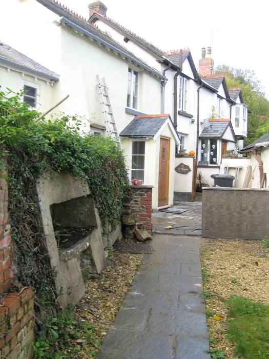 Approaching the well - on the left - along an access lane leading off the main west-east road through the village.
The original well is covered by the metal plate and a new, far too modern, concrete aperture had been constructed to hold the basin.  There's no water in it now, just  sediment. 