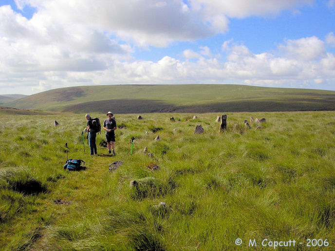 Kiss-in-the-Ring stone circle, seen here looking south, with the southern end of the longest known prehistoric stone row (more than 3 km in length) leading to it in the foreground. 

In the distance of the picture is Stalldown Barrow hill, with the wonderful Stalldon Row marching over its summit, which can be seen clearly in real life. 

The river Erme valley is to the left of the picture.