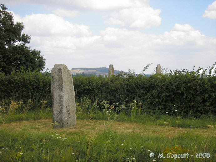 Just outside the main field of stones, beside the road junction, is a sixth menhir, this one only about 2 metres tall and broken, and which does not align with any of the others. Another stone is nearby.  

This is the first view you get of the stones as you approach. 