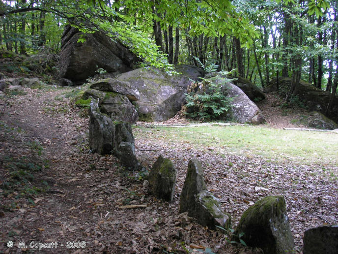 At the southern, upslope side, is a large outcrop of natural rocks, probably 10 to 15 metres high from which the cromlech extends in both directions. 