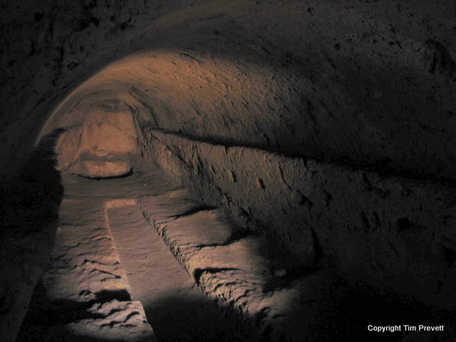 Cave 7 is a squeeze to enter. Muddy hands, knees and shins will be gained! Two small rectangular apertures linked by a small passage give entry to a very long carved out chamber, with a long thin rectangle cut into the centre, and a circular pit about three feet deep at the furthest end. My sun hat fell into the pit, and I had to climb in to retrieve it. I didn’t particularly relish that, but it