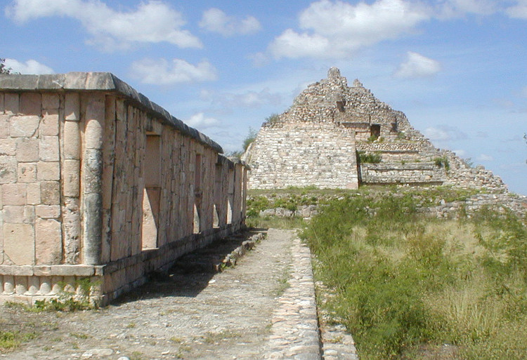 Oxkintok Structure MA-9 with the pyramid in the background.Building MA-9 bounds the north part of the Southeast Plaza of the Ah May Group. Its principal facade, which look to the north, extends out excessively because a large open esplanade, constituting the Northeast Plaza, was found in front of it.Building MA-9 is a palace-type and was built during the Terminal Classic period (750-1050 A.D.), final era o