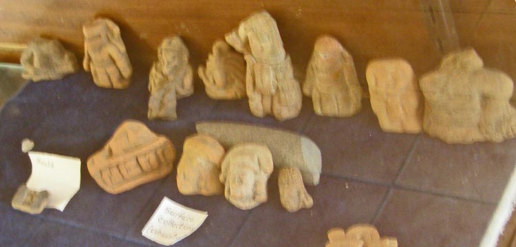 Original ceramic figurines and whistles displayed at the small museum on site at Lubaantun.  This is a very small fraction of the total hoard discovered. Note the presence of human forms (some in Mayan head dress) and geometric shapes.