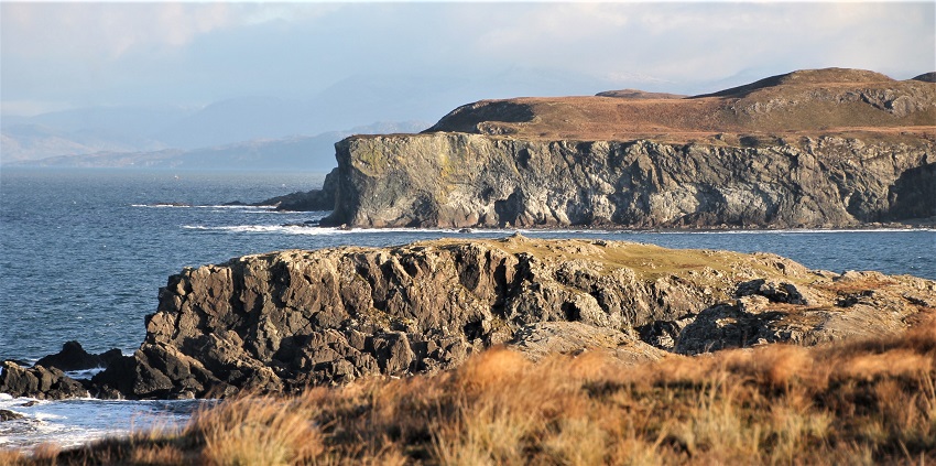 Looking from the west, the flattish top of the fort can be seen against the inlet. The cliff across the inlet is steeper than vertical at its northern end and clearly recognisable as one travels down the road from Achnaha to Sanna.