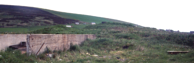 Finstown end of road.
Going into Finstown is the road to Evie. Go out of town and you can't miss the pillbox. This sits on The Hillock (RCAHMS NMRS Record no.HY31SE 4). I spent two seasons based just outwith, whilst working on The Howe outside Stromness, and I never realised I had a broch practically on my doorstep. At the near end is a space going down to the shore. To the left is a square moder