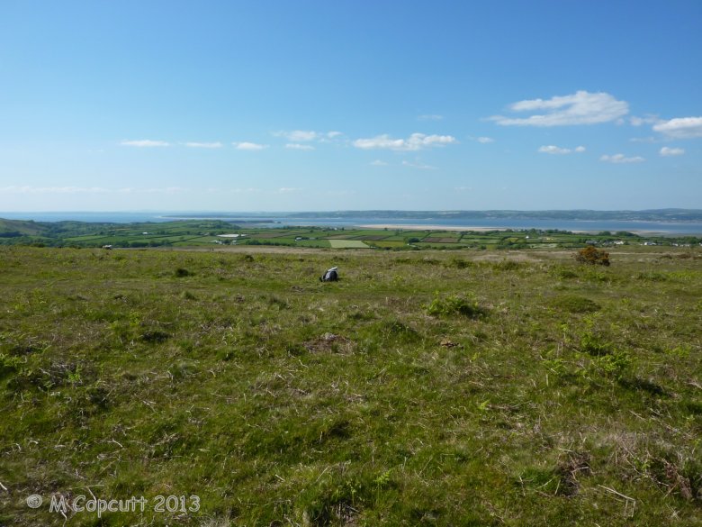 A few hundred metres to the northwest of the Trig Point on top of Cefn-Bryn can be found what looked to me to be the remains of a ring cairn, but may in fact be a denuded platform or round cairn. 

Viewed here looking northwest across the northwest coast of the Gower peninsula towards Burry Port on the far side of the River Loughor estuary. 