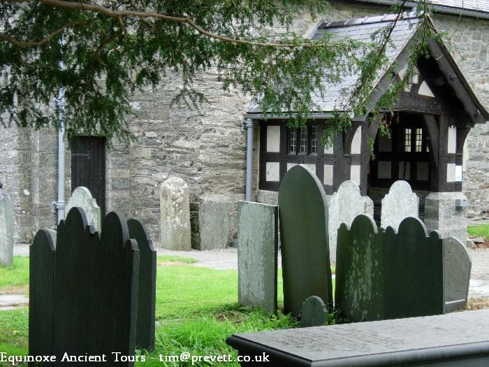 The smooth, cylindrical shape of Maen Twrog. This stone, not from the locality, was reputed to have been thrown from a nearby mountainside by the giant St Twrog, smashing a Pagan altar upon landing. His hand prints are supposed to be the indentations upon the top of the stone Ancient yews are in this churchyard, and the church, instead of having the usual church bells, has Tubular Bells. The Churc