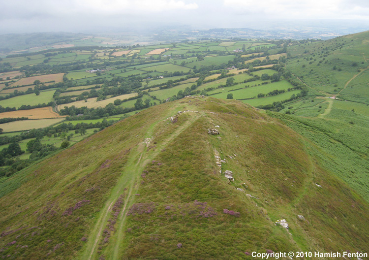 Cockit Hill (promontory fort/enclosure) viewed from the south. In the foreground the bank is visible by the fact that the heather is flowering on it. beyond the bank the interpretation of the fort is that it only extends around the nearest rock outcrops. 

To the right of the picture a path comes up the hillside to the end of the rampart/bank - there appears to be some small steps cut into the r